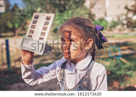 Retro device, soviet stereoscope, stereo vision. Cute girl watching 3D pictures with vintage slide viewer on the playground, past and future, happy moments and recollections