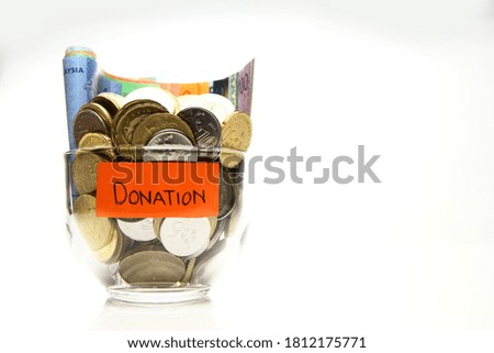 A full glass of coins and Malaysian Banknote (MYR) in white background. / Saving for donation, emergency, education, travel, and insurance