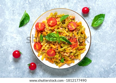 Fusilli - classic italian pasta from durum wheat with chicken meat, tomatoes cherry, basil in tomato sauce in white bowl on gray concrete table Mediterranean cuisine Top view Flat lay