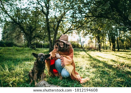 Portrait of a young happy beautiful blonde woman in a brown hat and orange plaid walks and play with dog in the autumn sunny park at sunset. Inspiration, autumn mood, travel, beauty of nature, forest.