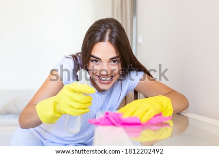 Beautiful young woman makes cleaning the house. Girl rubs dust. Smiling woman wearing rubber protective yellow gloves cleaning with rag and spray bottle detergent. Home, housekeeping concept.
