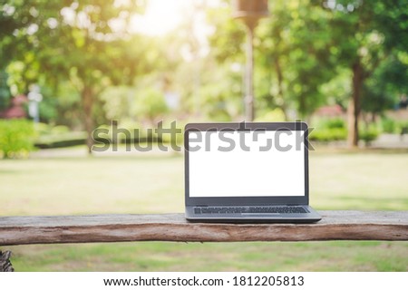 A silver laptop with a blank screen. Placed on an outdoor wooden table for a park tree backdrop.