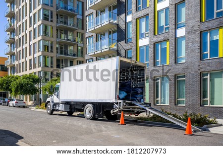 Industrial Medium-sized professional Big rig day cab semi truck with box trailer unloading delivered cargo standing on the urban city street with multilevel residential apartment buildings
 Royalty-Free Stock Photo #1812207973