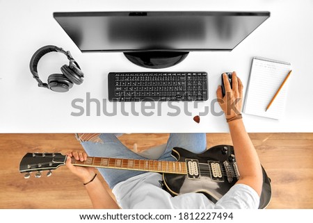 leisure, music and people concept - young man or musician with computer and guitar sitting at table