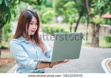 Asian female office worker using laptop or computer  notebook in the park She wears a blue shirt.