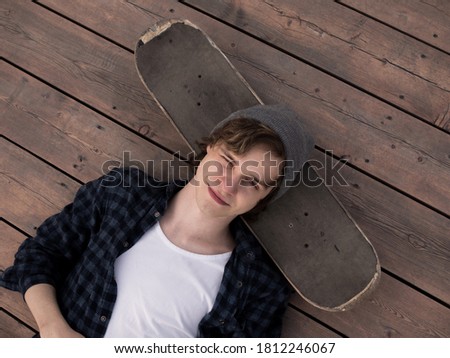 Young man is smiling and lying on the wood floor with skateboard