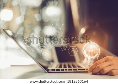 Business woman Hand holding Light bulb in office,with icons holographic,in office blurred background.