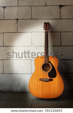 Acoustic guitar leaning on grungy gray brick wall