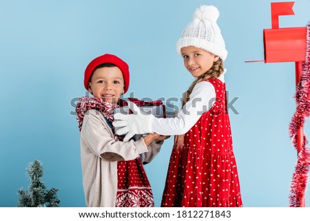 sister and brother in winter outfit holding present near mailbox on blue