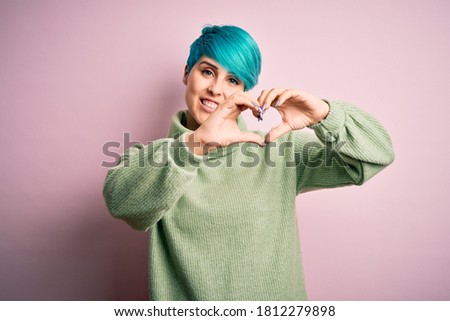 Young beautiful woman with blue fashion hair wearing casual turtleneck sweater smiling in love showing heart symbol and shape with hands. Romantic concept.
