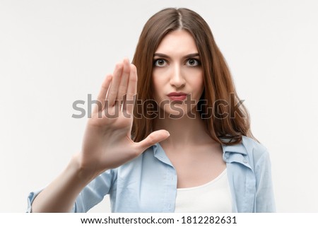 Serious woman with long chestnut hair, dressed in casual clothes shows a stop with her hand, showing symbol of rejection, not allow violence, body language. Human emotions, facial expression concept.