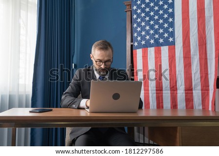 Smiling business vintage, white gentleman, Caucasian person with american or usa national flag working from home on table with computer notebook laptop on webcam video call conference in quarantine.