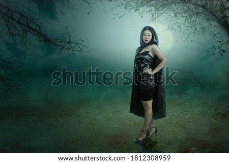Asian witch woman with a cloak standing with a haunted forest background