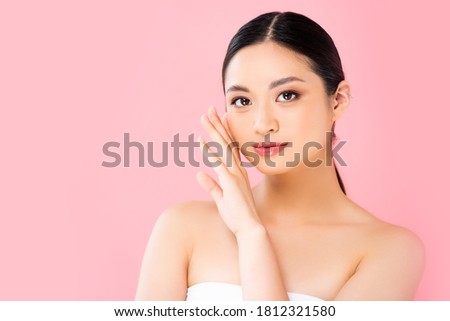 young asian woman looking at camera and touching face isolated on pink