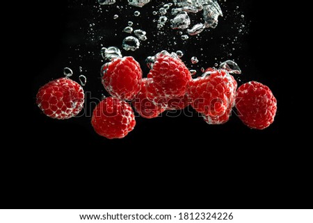 Raspberries splashing into clear water isolated on black background. Healthy fruits concept. Copy space