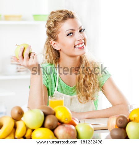 Beautiful young woman in the kitchen, holding an apple. Looking at camera.