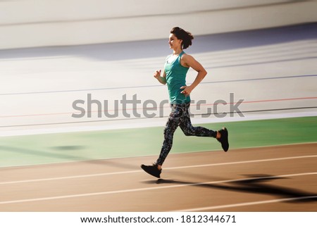 Sporty young woman running by red all-season track at the stadium. Motion blurred photo