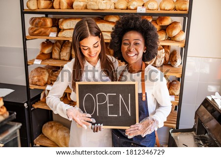Young business women holding an open sign. Bakery shop female owner showing chalkboard with open sign while opening store. Local business, hospitality, open after lockdown concept.