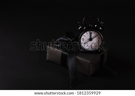 Black Friday sale shopping concept, Top view of gift box wrapped in black paper and black bow ribbon and black alarm clock, studio shot on dark background