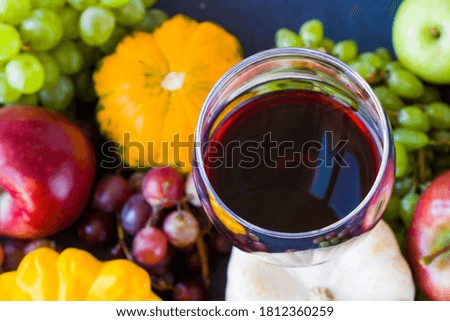 Full red wine glass and autumn and fall harvest, pumpkin, apple and grape on the blue background