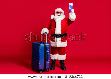 Full length photo of retired old man white beard hold suitcase tickets prepare flight abroad wear x-mas santa costume glove coat belt sunglass cap boot isolated red color background