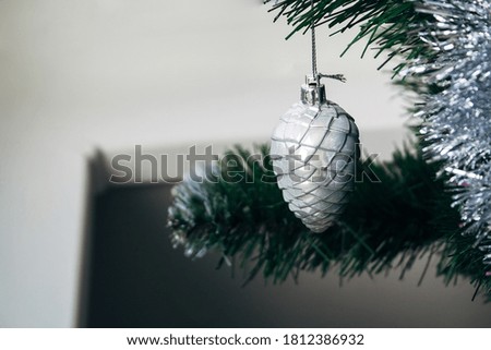 Silver white toy cone hanging on artificial Christmas tree with copy space. Selective focus. Holiday card with decorations for the New Year's Eve