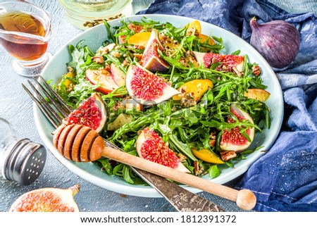 Autumn fig and arugula salad recipe. Whole vegan paleo fruit and vegetable fall salad idea. Homemade salad bowl with figs, arugula, peach and apple slices, nuts and honey. 