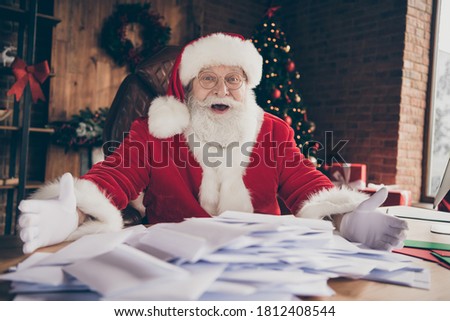 Crazy santa claus amazed impressed many receive wish list letters showing sit table wear cap headwear in house indoors with christmas x-mas lights decoration