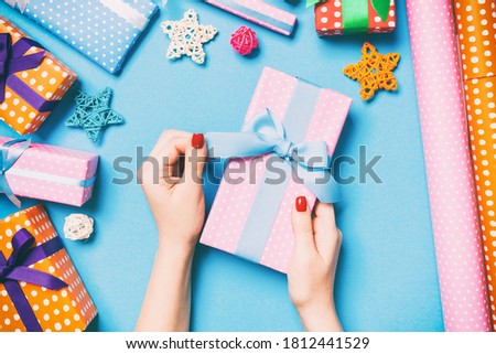 Top view of female hands holding a Christmas present on festive blue background. Holiday decorations and wrapping paper. New Year holiday concept.