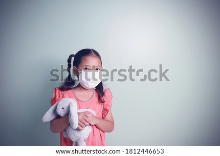 Portrait asian cute kid girl wearing a white mask for protection virus and dust standing huggy a rabbit doll on the green background with copy space.