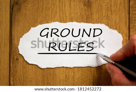 Male hand writing 'ground rules' on white paper on wooden table. Business concept.