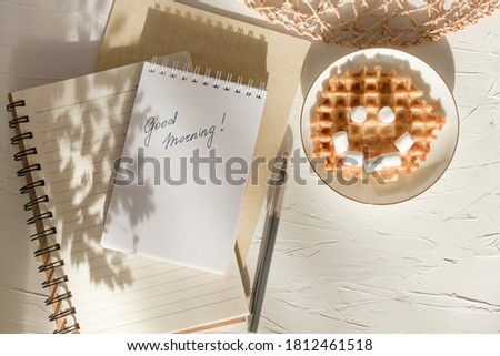 Marshmallow waffle smile and greeting card with the inscription good morning on white textured table. Flat composition. Funny breakfast.
