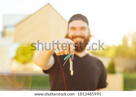Selective focus on keys, close up photo of smiling young man holding HOUSE KEYS outdoor at sunset