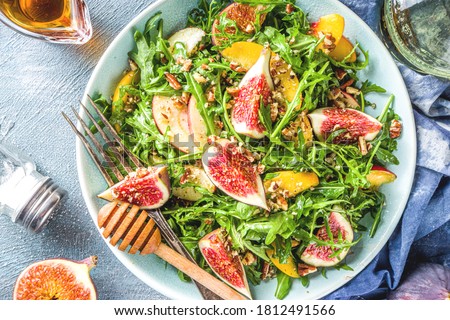 Autumn fig and arugula salad recipe. Whole vegan paleo fruit and vegetable fall salad idea. Homemade salad bowl with figs, arugula, peach and apple slices, nuts and honey.  Royalty-Free Stock Photo #1812491566