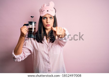 Young brunette woman with blue eyes wearing pajama making coffee with french coffeemaker pointing with finger to the camera and to you, hand sign, positive and confident gesture from the front