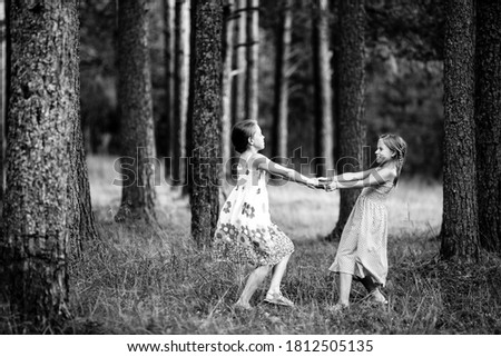 Two little girls for the holding hands in the pine forest. Black and white photo.