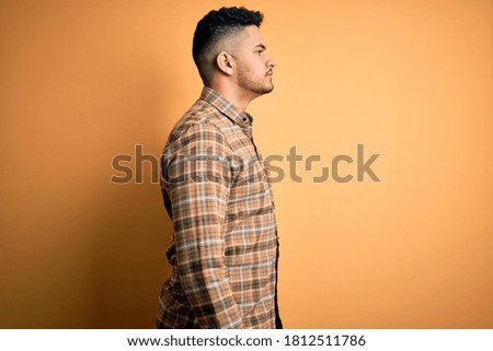 Young handsome man wearing casual shirt standing over isolated yellow background looking to side, relax profile pose with natural face and confident smile.
