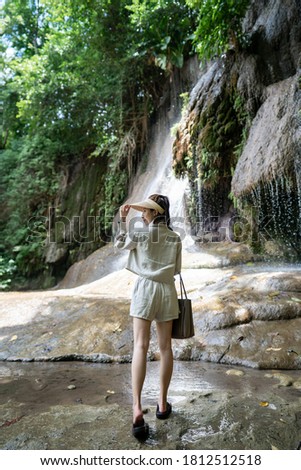 Back side of woman with waterfall in tropical rainforest with rock. Saiyok noi Waterfall, Located in Kanchanaburi province, Thailand. 