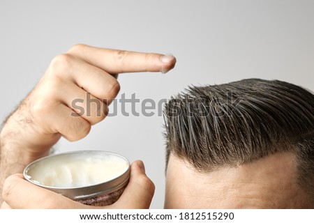 Man applying a clay, pomade, wax, gel or mousse from round metal box for styling his hair after barbershop hair cut. Advertising concept of mans products. Treatment and care against lost of hair Royalty-Free Stock Photo #1812515290