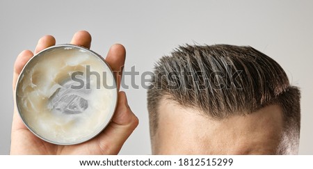 Man applying a clay, pomade, wax, gel or mousse from round metal box for styling his hair after barbershop hair cut. Advertising concept of mans products. Treatment and care against lost of hair Royalty-Free Stock Photo #1812515299