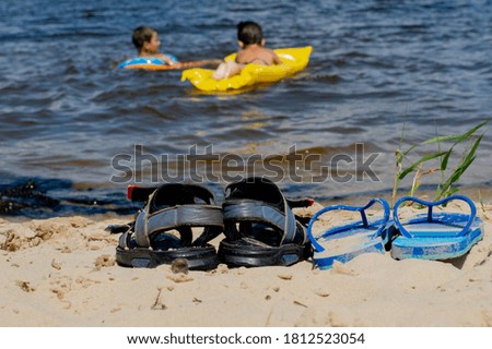 On a hot summer day, children swim in the river. Children's shoes on the beach.