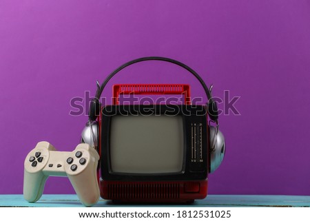Retrogaming. Video game competition. Old TV with headphones and gamepad on purple background. Attributes 80s