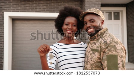 Portrait of young African American maried couple of army soldier standing in hugs outdoor at home, smiling and showing key to camera.