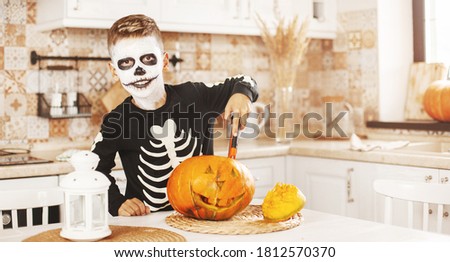 Happy boy at home in the kitchen in Halloween costumes and makeup, carves a pumpkin, plays and laughs.