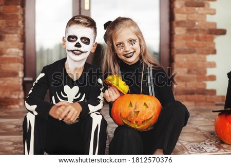 Happy kids celebrate halloween on the street near the house in costumes and make-up with pumpkin lantern jack,