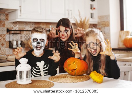 Happy kids celebrate halloween in kitchen at home in costumes and make-up with pumpkin lantern Jack looking at camera and smiling. Preparing for Halloween.