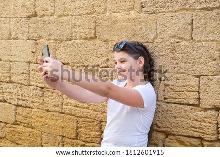 Stylish teenager girl takes a selfie in city over stone wall background.
