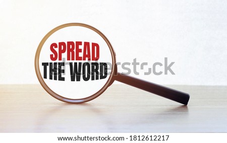 Magnifying glass with text SPREAD THE WORD on wooden table.