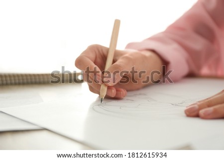 Woman drawing girl's portrait with pencil on sheet of paper at table, closeup