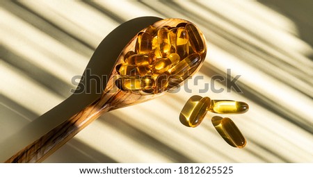 Cod liver oil capsules with vitamin D in the wooden spoon on light beige background with hard shadows. Health care concept.